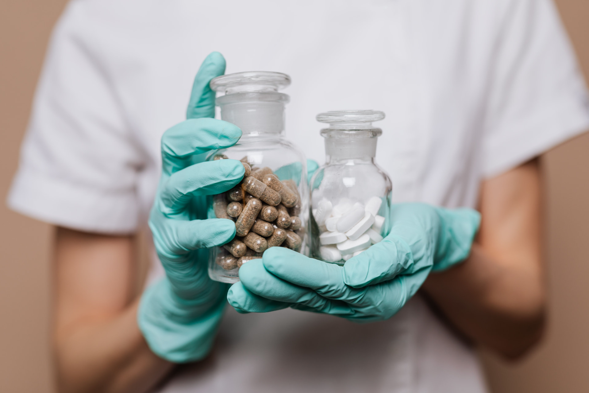 Gloved hands holding glass bottles of specialty medication capsules and tablets